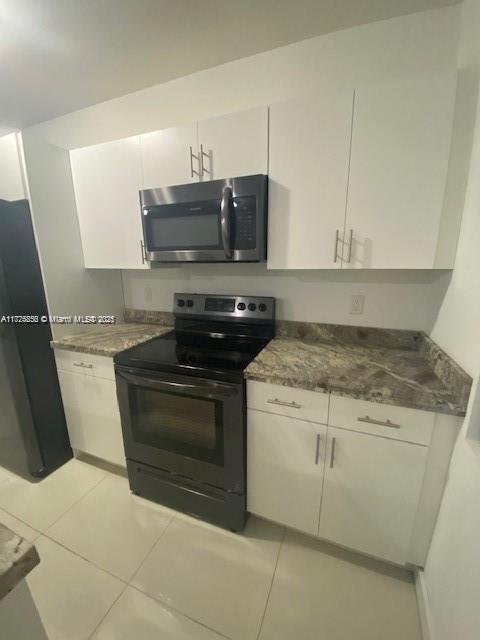 kitchen with white cabinetry, light tile patterned floors, range with electric stovetop, and dark stone counters