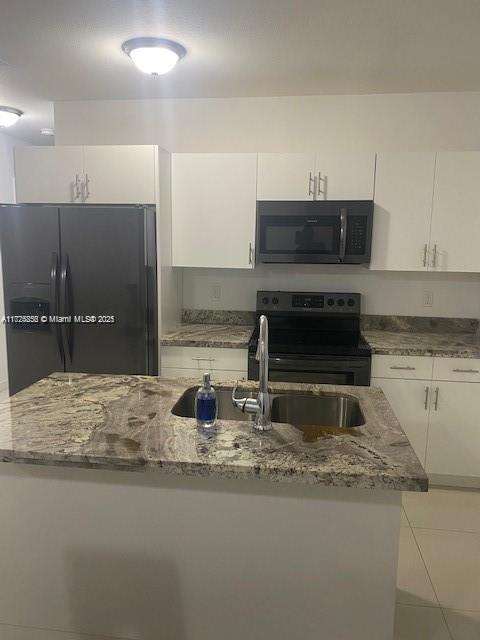 kitchen featuring black appliances, dark stone counters, white cabinets, and light tile patterned floors