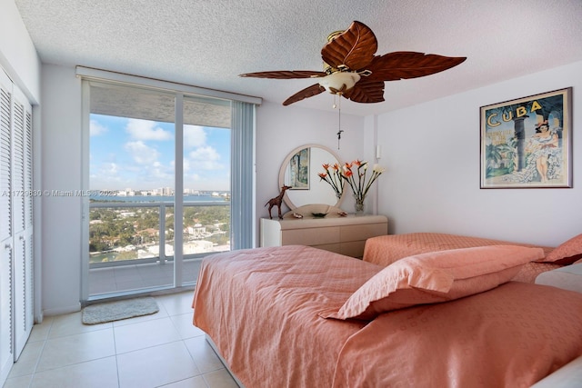 tiled bedroom with ceiling fan, a wall of windows, access to exterior, and a textured ceiling