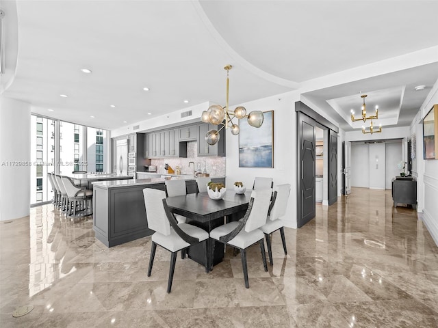 dining room with a raised ceiling, sink, and an inviting chandelier