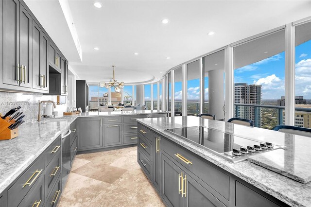 kitchen featuring sink, gray cabinetry, light stone countertops, black electric cooktop, and decorative light fixtures