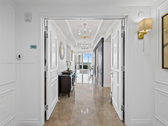 hall with a tray ceiling and a chandelier