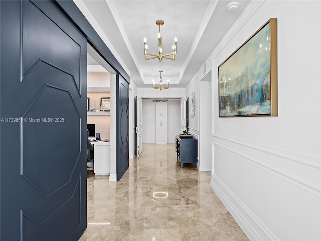 hallway with an inviting chandelier and a raised ceiling