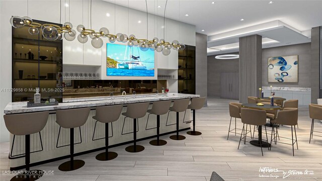 kitchen featuring white cabinetry, light stone counters, pendant lighting, and a kitchen bar