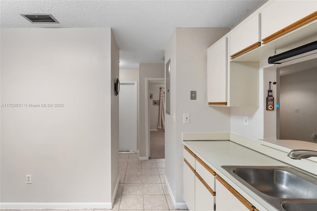 kitchen with sink, light tile patterned flooring, white cabinets, and a textured ceiling