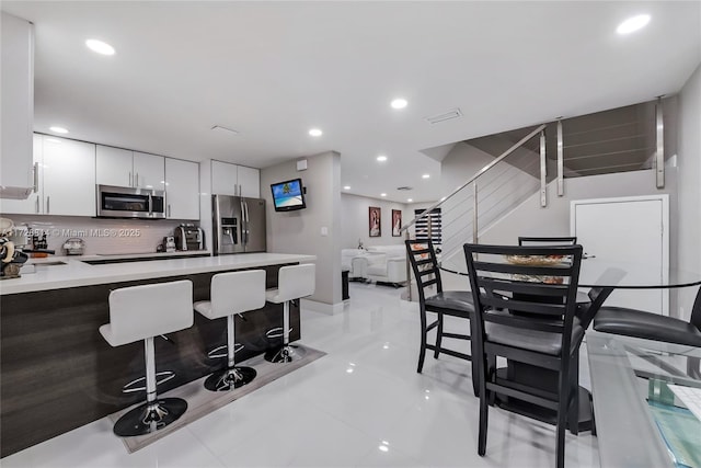 kitchen with white cabinetry, light tile patterned floors, a kitchen breakfast bar, backsplash, and stainless steel appliances