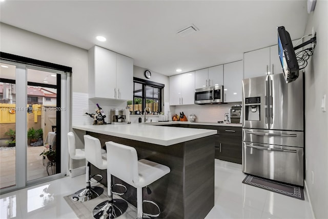 kitchen with white cabinetry, stainless steel appliances, decorative backsplash, light tile patterned flooring, and a breakfast bar area