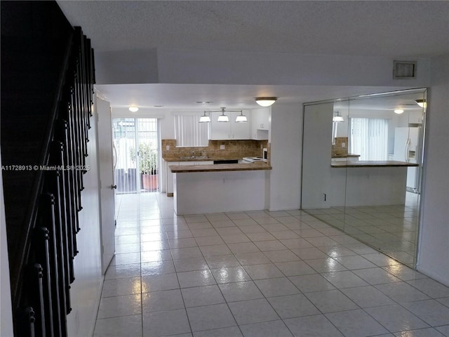 kitchen with light tile patterned floors, sink, white cabinetry, white fridge with ice dispenser, and kitchen peninsula