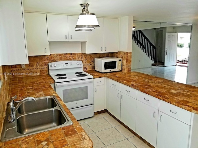 kitchen featuring white appliances, sink, hanging light fixtures, and white cabinets