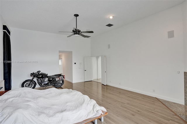 bedroom featuring light wood-type flooring, ceiling fan, and a towering ceiling