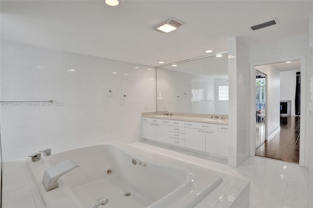 bathroom featuring a relaxing tiled tub, tile walls, tile patterned floors, and vanity