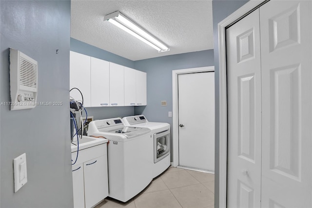 laundry area with light tile patterned flooring, cabinets, a textured ceiling, and washing machine and dryer