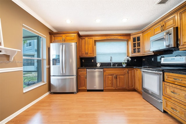 kitchen with decorative backsplash, appliances with stainless steel finishes, brown cabinets, light wood-style floors, and a sink