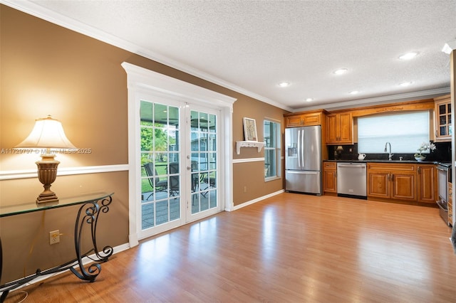 kitchen featuring brown cabinetry, dark countertops, light wood-style flooring, appliances with stainless steel finishes, and ornamental molding