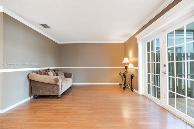 sitting room with baseboards, light wood finished floors, visible vents, and crown molding