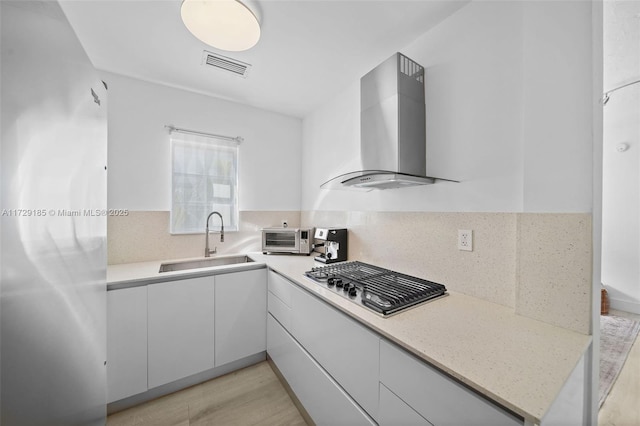 kitchen with wall chimney exhaust hood, decorative backsplash, sink, light hardwood / wood-style floors, and stainless steel gas cooktop