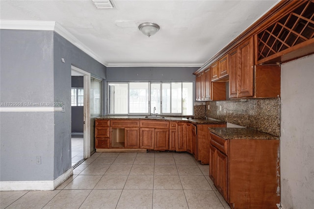 kitchen with light tile patterned floors, sink, ornamental molding, backsplash, and dark stone counters