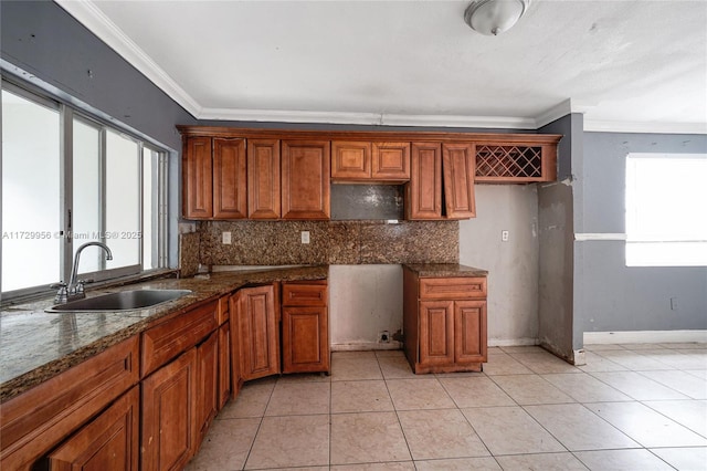 kitchen with dark stone countertops, sink, backsplash, ornamental molding, and light tile patterned floors