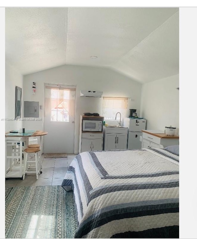 bedroom featuring sink, lofted ceiling, white fridge, and light tile patterned flooring