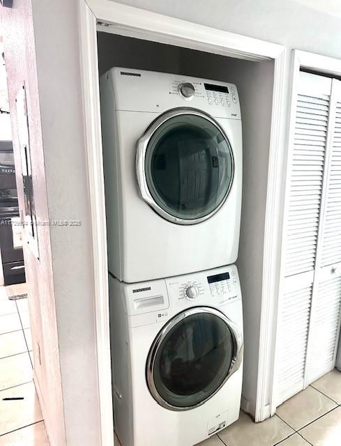 clothes washing area with light tile patterned floors and stacked washing maching and dryer