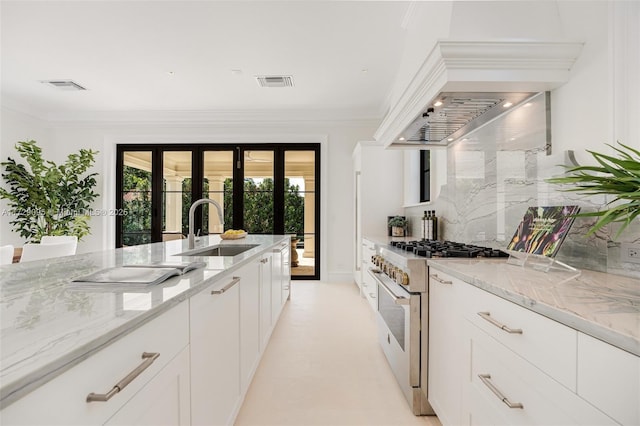 kitchen featuring light stone countertops, white cabinets, custom exhaust hood, stainless steel range, and sink