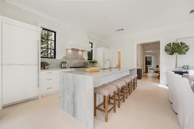 kitchen featuring white cabinets, sink, light stone counters, crown molding, and a breakfast bar area