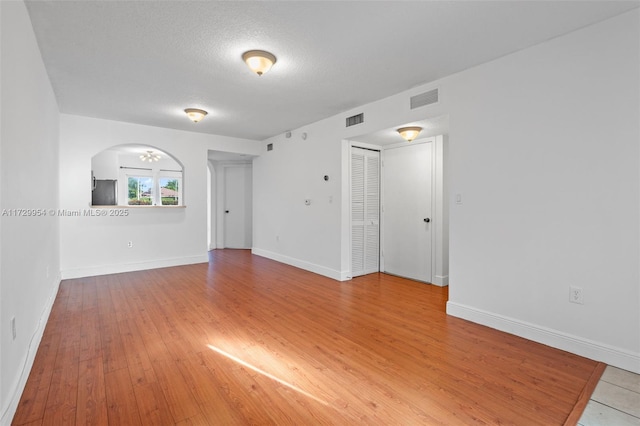 spare room with light wood-style floors, arched walkways, visible vents, and baseboards