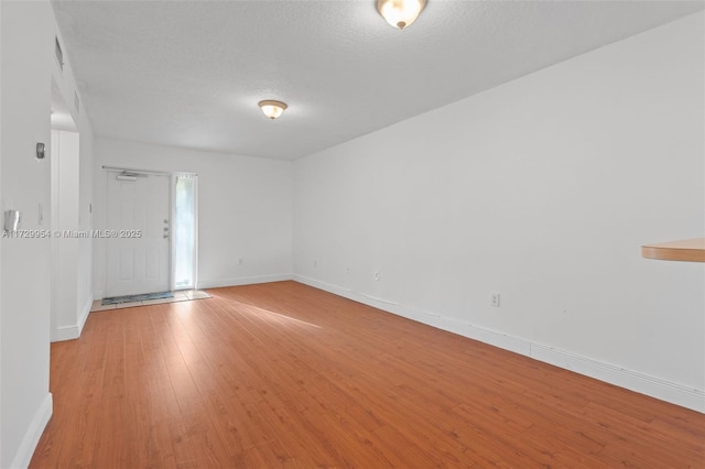 empty room featuring visible vents, light wood-style flooring, a textured ceiling, and baseboards