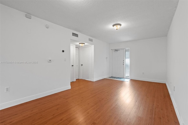 empty room with visible vents, baseboards, a textured ceiling, and light wood-style flooring