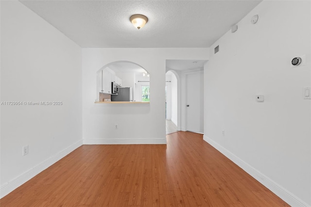 empty room with visible vents, a textured ceiling, arched walkways, light wood-style floors, and baseboards