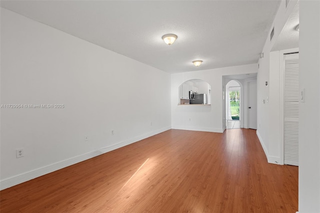 unfurnished room with wood finished floors, visible vents, baseboards, arched walkways, and a textured ceiling