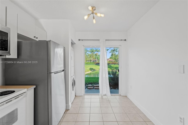 kitchen featuring stacked washer and dryer, white cabinetry, white electric stove, light tile patterned floors, and baseboards