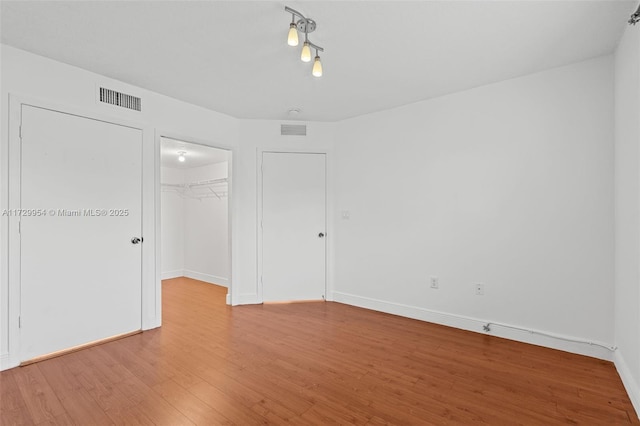 unfurnished bedroom featuring a spacious closet, visible vents, a closet, and light wood-style floors