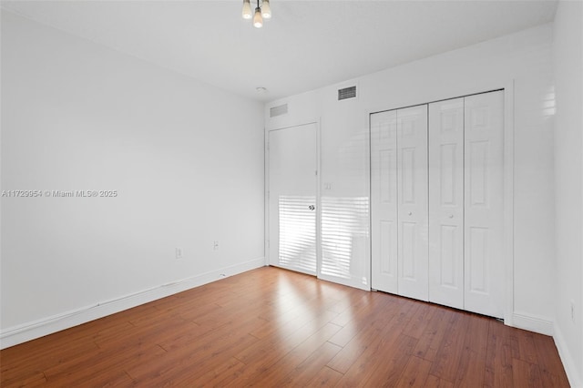 unfurnished bedroom with visible vents, wood finished floors, baseboards, and a closet