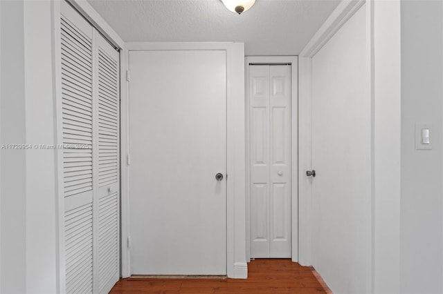 hallway with a textured ceiling and wood finished floors