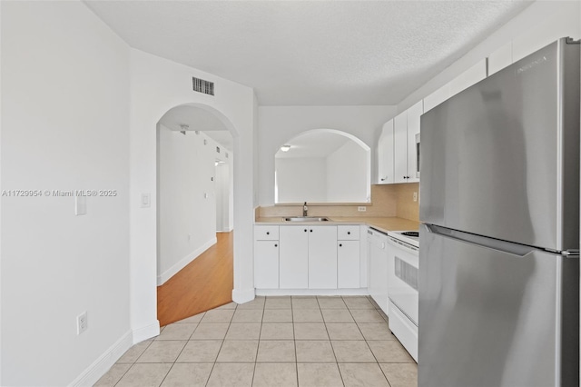 kitchen with visible vents, freestanding refrigerator, a sink, light countertops, and electric stove