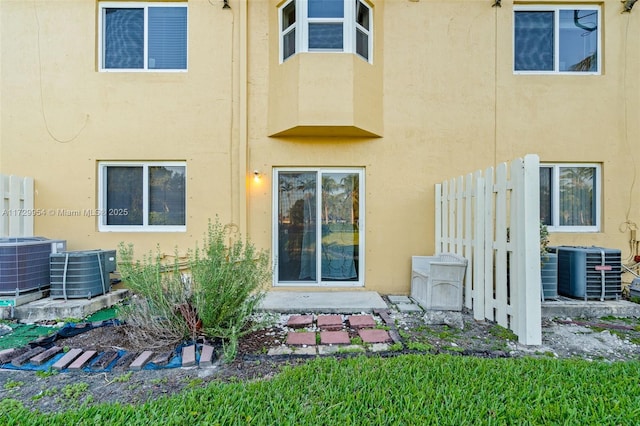 back of house featuring central AC unit, fence, and stucco siding