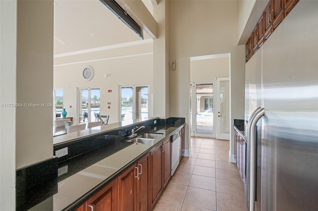 kitchen featuring light tile patterned floors, brown cabinetry, a sink, a towering ceiling, and appliances with stainless steel finishes