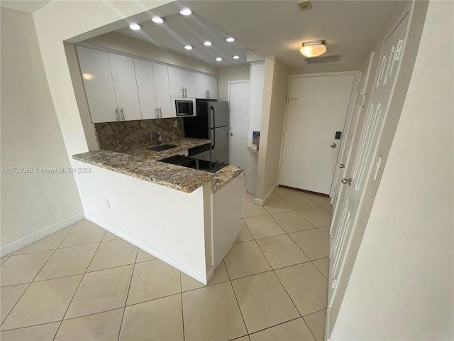 kitchen with white cabinets, appliances with stainless steel finishes, tasteful backsplash, stone countertops, and kitchen peninsula