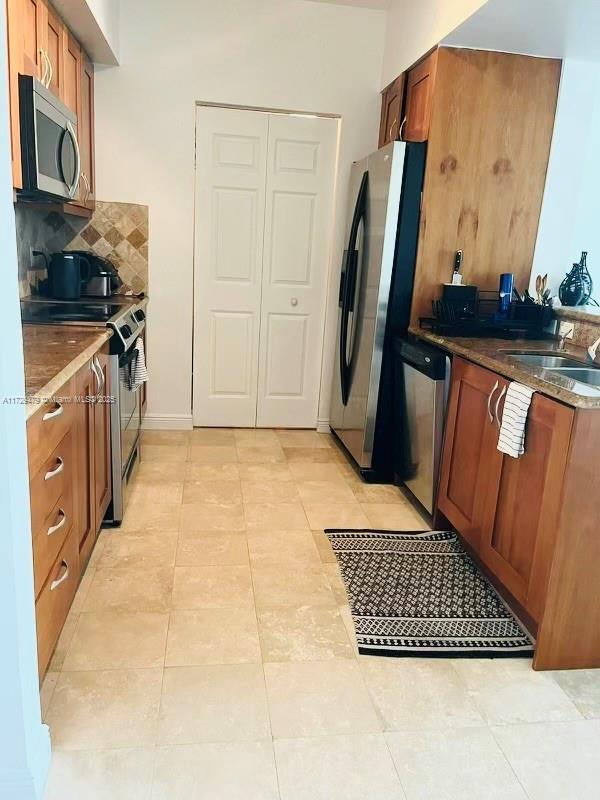 kitchen with brown cabinetry, stainless steel appliances, tasteful backsplash, and a sink