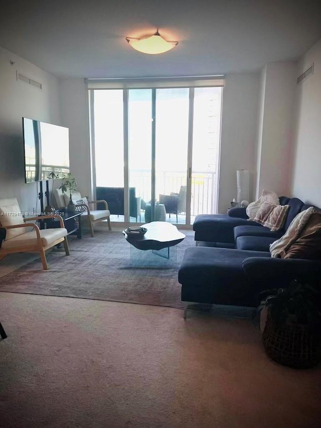 carpeted living area with a wealth of natural light, visible vents, and floor to ceiling windows