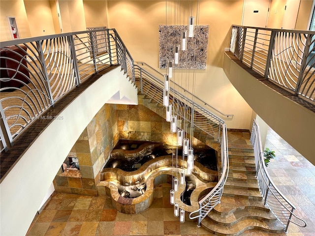 staircase featuring baseboards, a towering ceiling, and stone tile floors