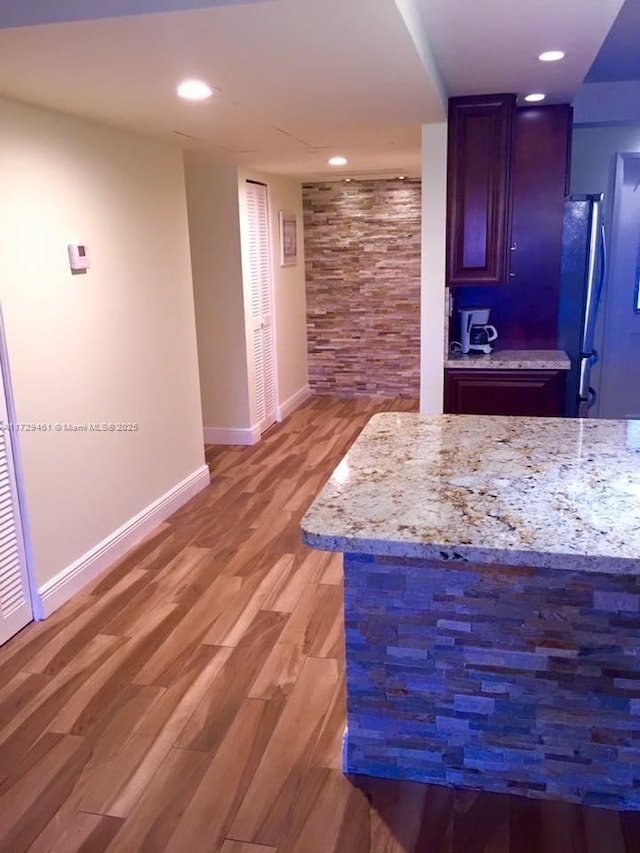 bar with hardwood / wood-style flooring, refrigerator, and light stone counters