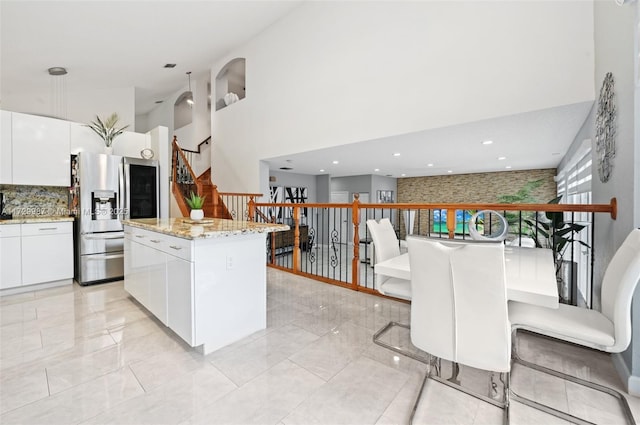 kitchen with stainless steel fridge with ice dispenser, a center island, white cabinets, and a high ceiling