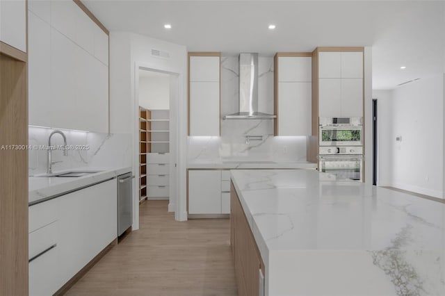 kitchen with wall chimney exhaust hood, backsplash, white cabinetry, and stainless steel appliances