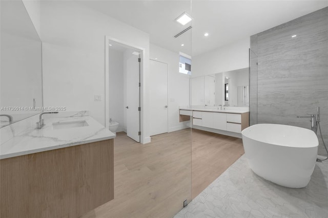 bathroom with tile walls, hardwood / wood-style floors, toilet, a bathing tub, and vanity