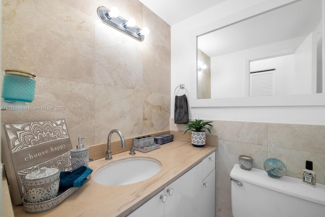 bathroom with toilet, vanity, and tile walls