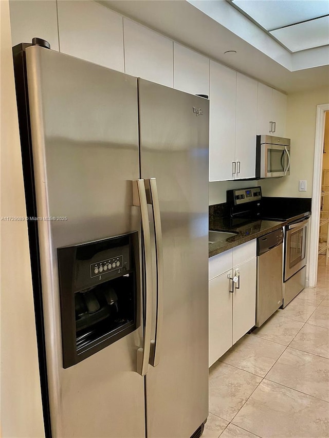 kitchen with appliances with stainless steel finishes, dark stone countertops, and white cabinets