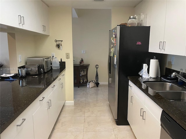 kitchen featuring sink, light tile patterned floors, white cabinets, stainless steel dishwasher, and dark stone counters