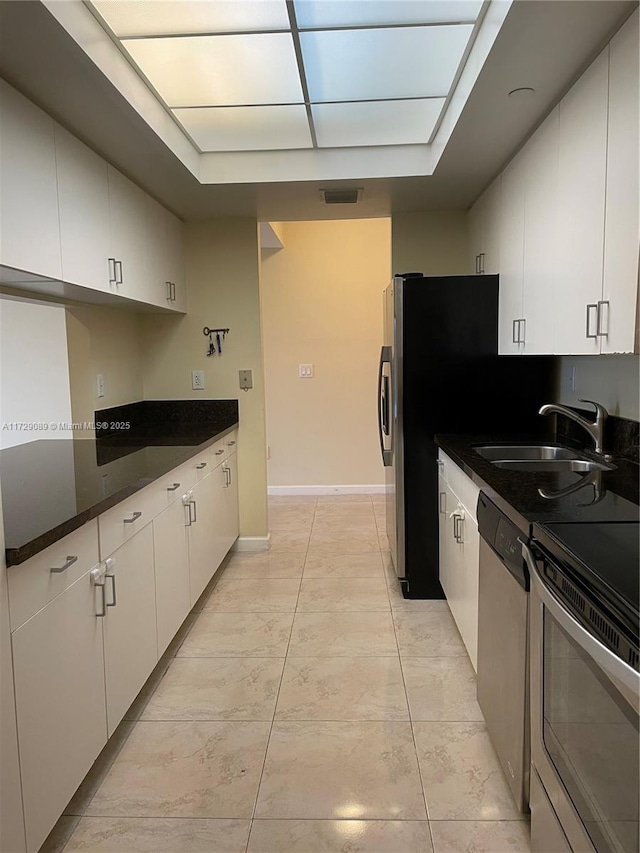 kitchen with white cabinetry, stainless steel appliances, sink, and dark stone countertops